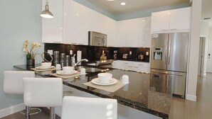 A modern kitchen with white cabinets, a stainless steel refrigerator, and a granite countertop. - 1507 Dream (Clermont)
