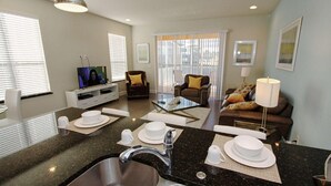 A modern kitchen with a granite countertop, stainless steel sink, and a dining area with white plates and bowls. - 1507 Dream (Clermont)