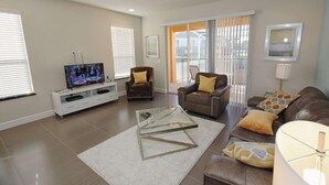 A modern living room with a glass coffee table, leather sofas, and a flat-screen TV. - 1507 Dream (Clermont)