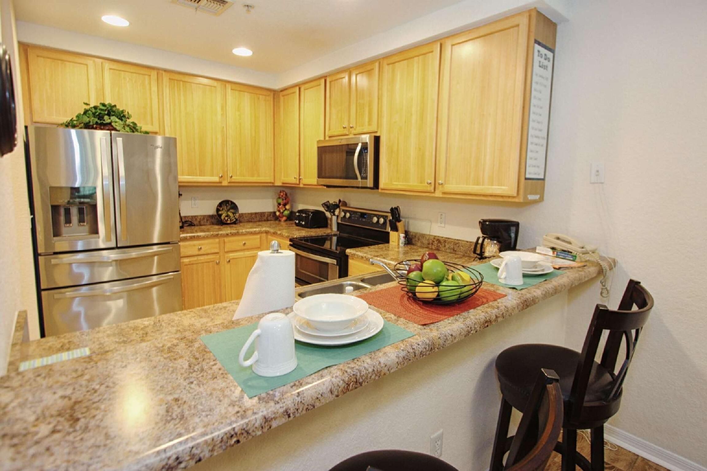 A kitchen with wooden cabinets, stainless steel appliances, granite countertops, and a breakfast bar with chairs.