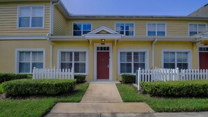 A two-story yellow building with a red door, white picket fence, and a small front yard with trimmed bushes. - 4562 Seven Dwarfs (Kissimmee)