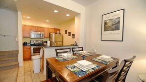 A dining area with a wooden table set for four, a kitchen in the background, and a framed picture on the wall. - 4562 Seven Dwarfs (Kissimmee)