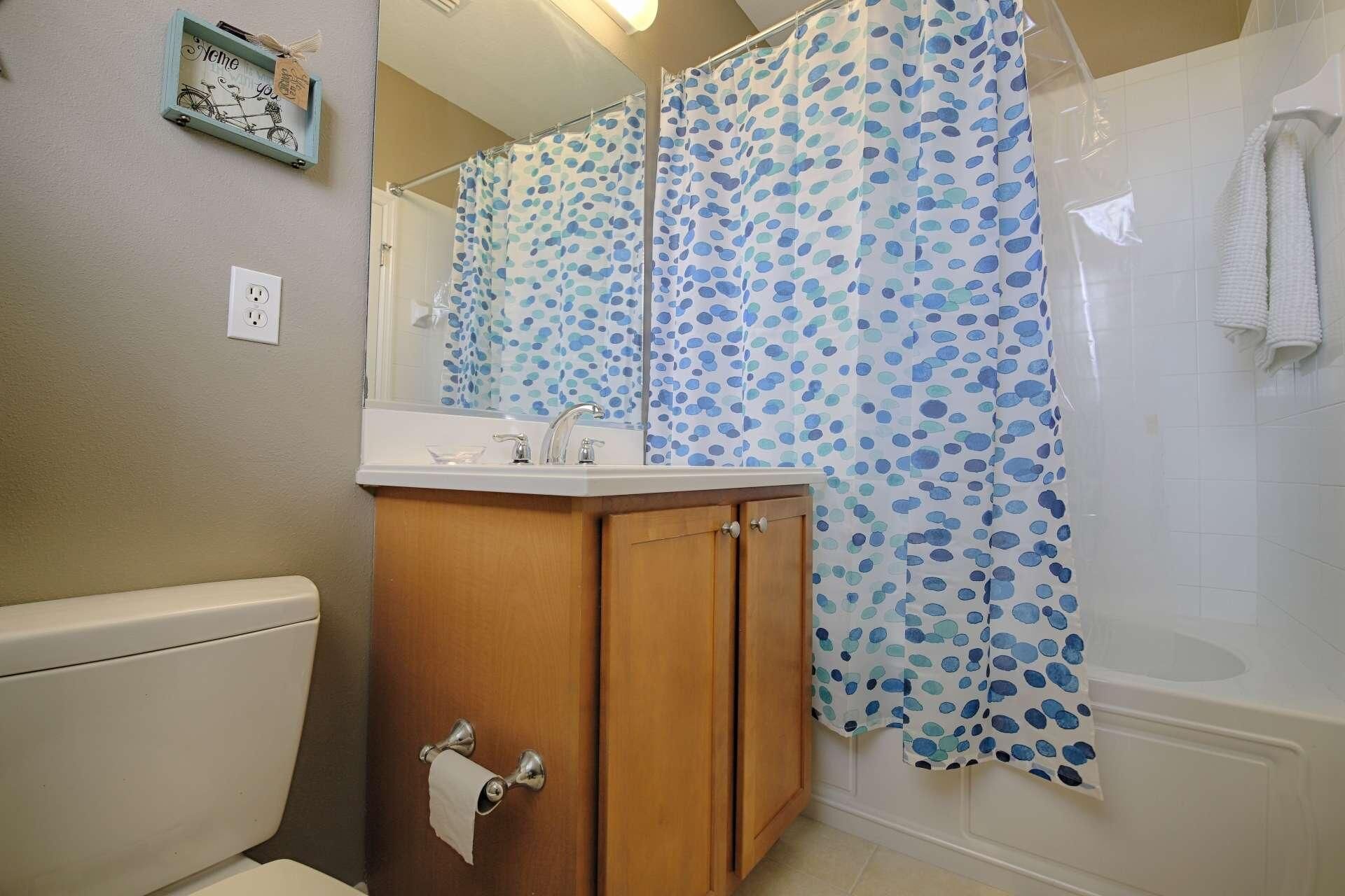 Un bagno con un armadietto in legno, un water, un lavandino e una doccia con tenda a pois.