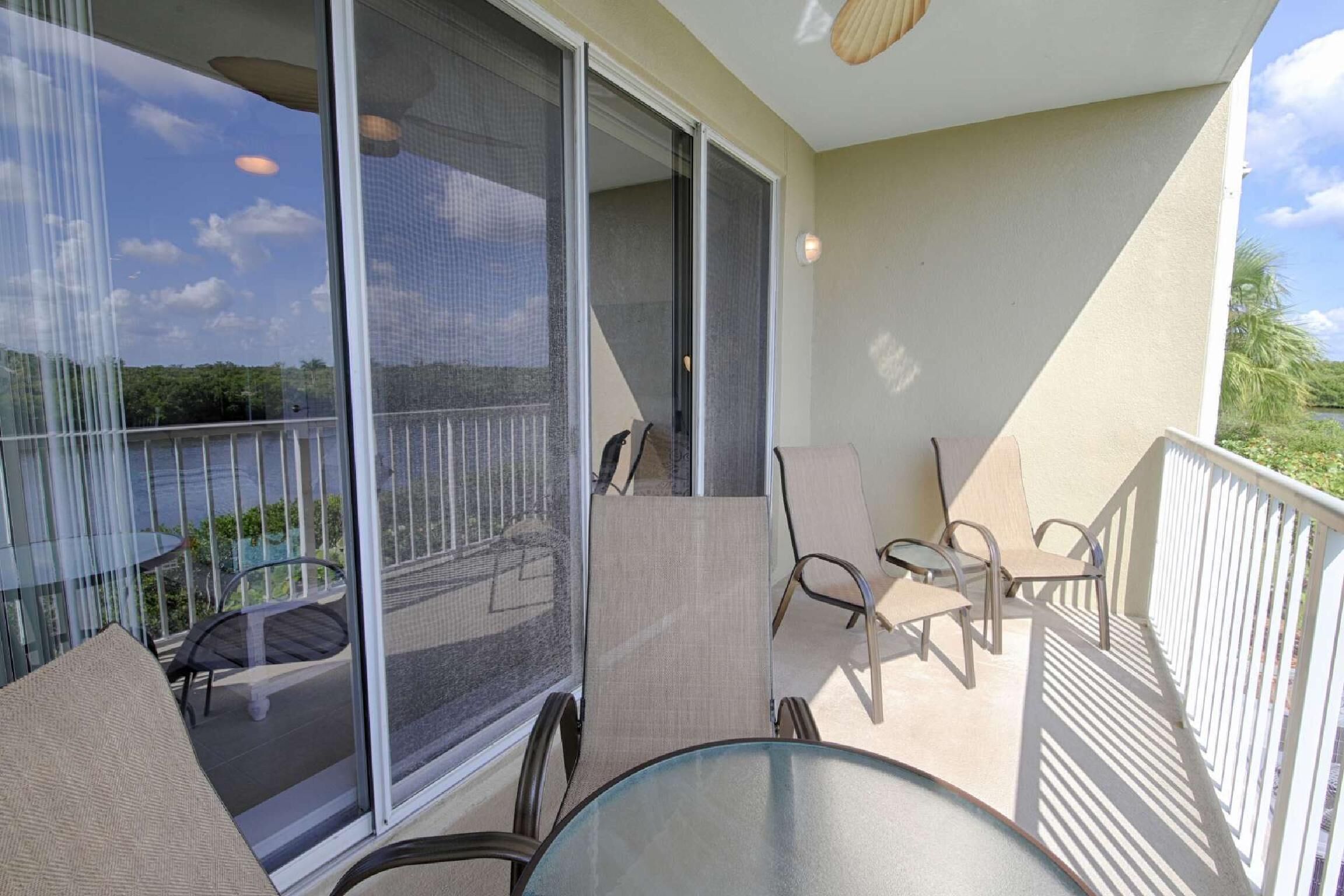 A balcony with a glass table and chairs, a sliding door, and a view of the outdoors.