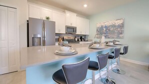 Una cocina moderna con armarios blancos, electrodomésticos de acero inoxidable y una isla central con taburetes de bar.