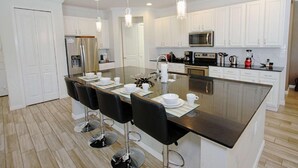 A modern kitchen with white cabinets, stainless steel appliances, a central island with bar stools, and pendant lighting. - 3941 Sonoma (Kissimmee)