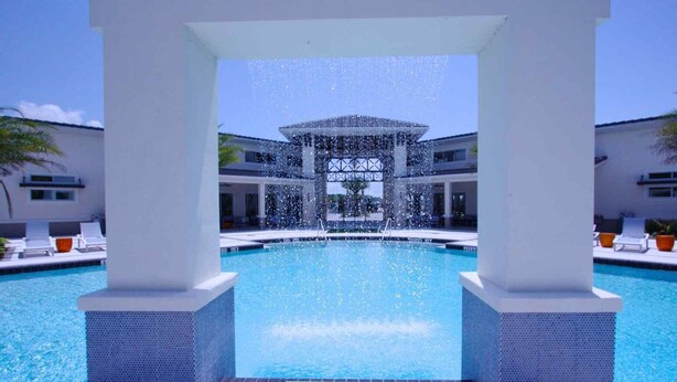 A swimming pool with a water feature in the center, surrounded by lounge chairs and a covered area. - 3941 Sonoma (Kissimmee)