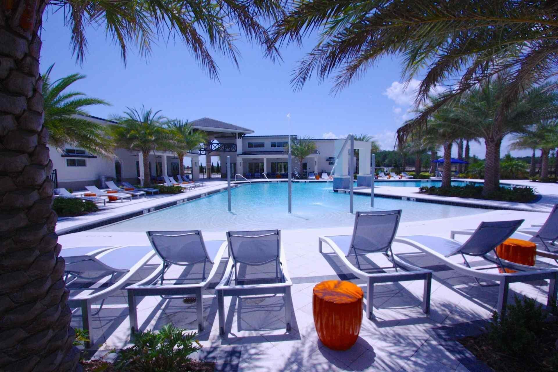 A pool area with lounge chairs, a modern building, and palm trees.