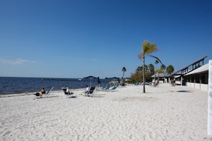 A beach with white sand, a few lounge chairs, and a building with a covered area.