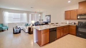 A modern kitchen with wooden cabinets, a built-in dishwasher, and a large island with a sink. - 5133 Compass Bay (Kissimmee)
