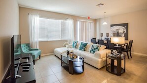 A living room with a sofa, a coffee table, a TV, and a dining area with a table and chairs. - 5133 Compass Bay (Kissimmee)