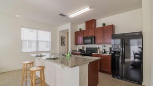 Una cocina moderna con una isla central, taburetes de madera, un refrigerador negro y un microondas.