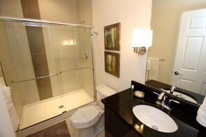 A modern bathroom with a glass-enclosed shower, a white toilet, a black countertop sink, and a mirror. - 1521 Dream (Clermont)