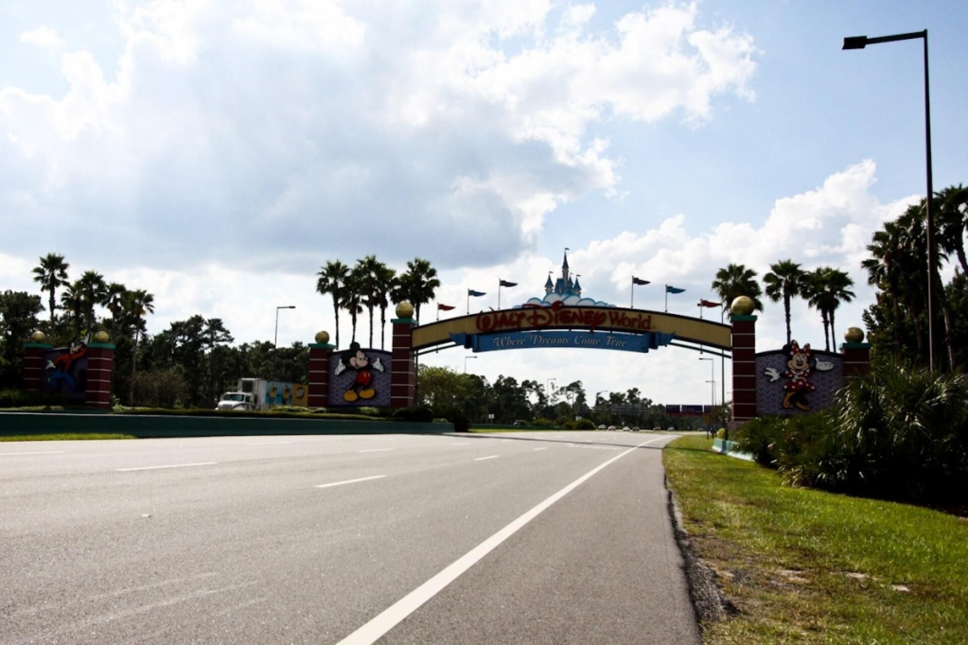 A road leading to a theme park entrance with a large archway featuring cartoon characters and the theme park's name.