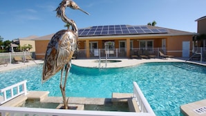 Une piscine ornée d’une sculpture d’oiseau, un bâtiment doté de panneaux solaires et un ciel d’un bleu limpide.