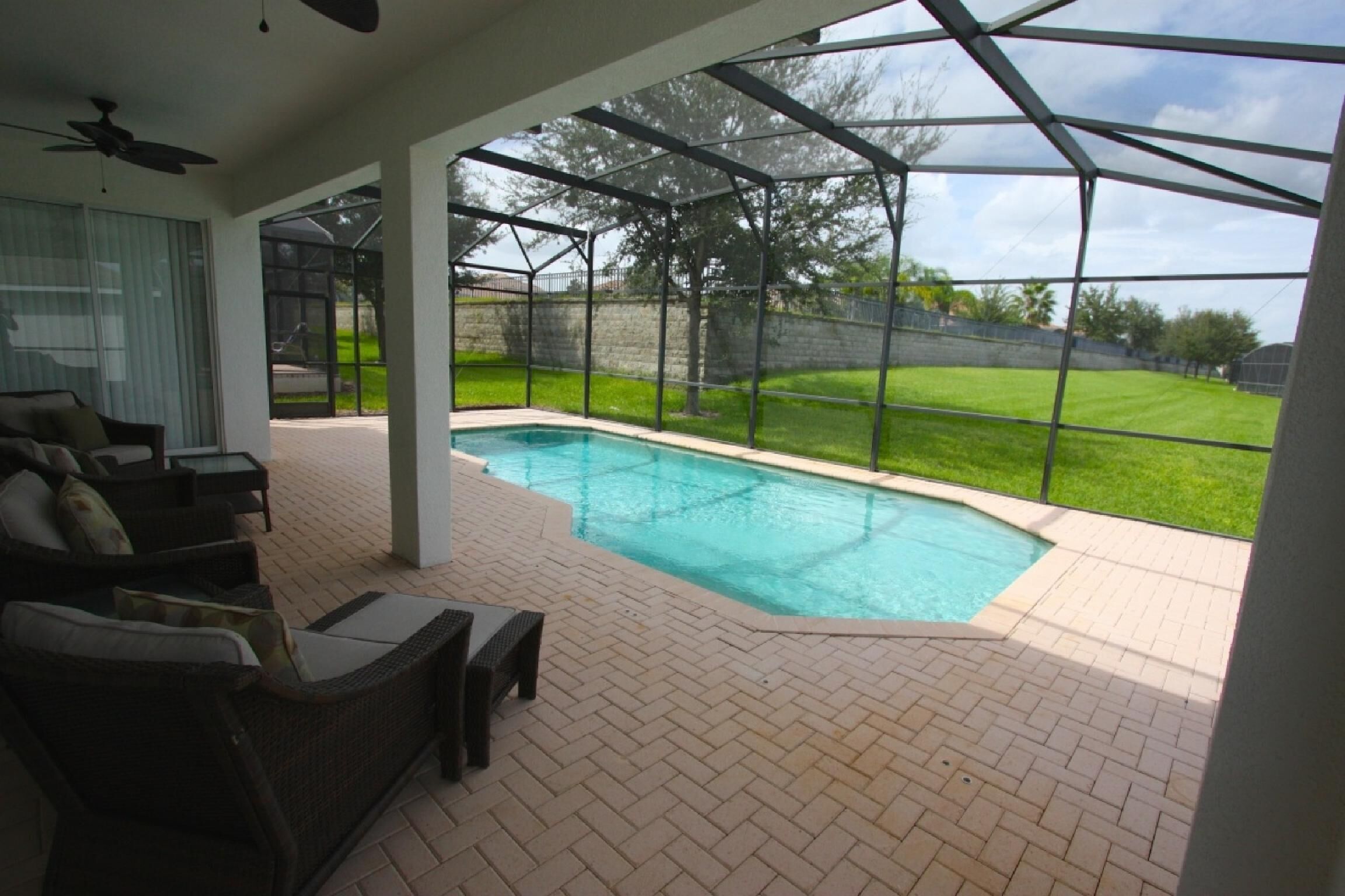 A covered outdoor area with a swimming pool, patio furniture, and a view of the backyard.