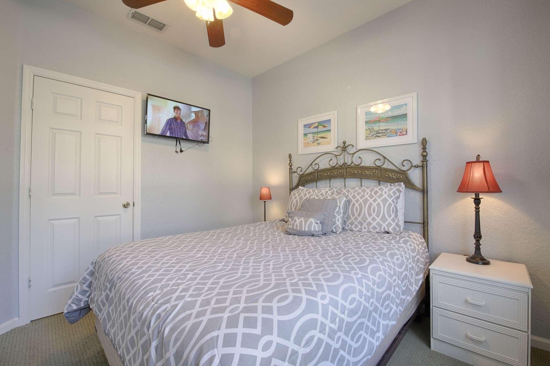 A bedroom with a bed, a nightstand, a lamp, a ceiling fan, a TV, and two framed pictures on the wall.