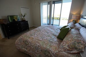 A bedroom with a large bed, a dresser, a television, and a balcony with a view. - 579 Little Harbor (Ruskin)