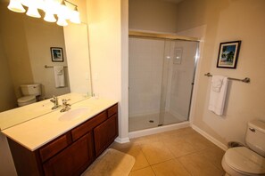 A bathroom with a white sink, wooden vanity, a glass shower enclosure, and a toilet. - 4114 Vista Cay (Orlando)