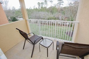 A balcony with two chairs and a small table, overlooking a grassy area with trees. - 863 Reunion (Kissimmee)
