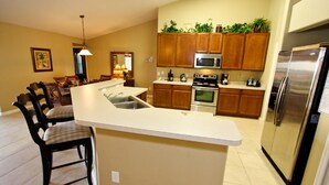 A modern kitchen with wooden cabinets, a stainless steel refrigerator, and a central island with seating. - 217 Legacy Park (Davenport)