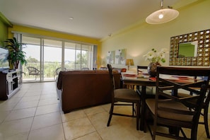 A dining area with a table, chairs, and a sofa. There is a TV on a stand and a plant in the corner. - 515 Little Harbor (Ruskin)