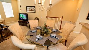 A dining area with a round glass table, beige upholstered chairs, and a chandelier. - 8036 Vista Cay 134 (Orlando)