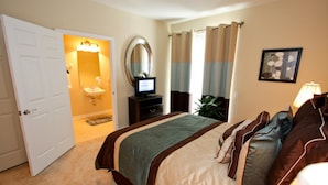 A hotel room with a bed, a television, a bathroom with a sink and mirror, and a door leading to another room. - 8036 Vista Cay 134 (Orlando)