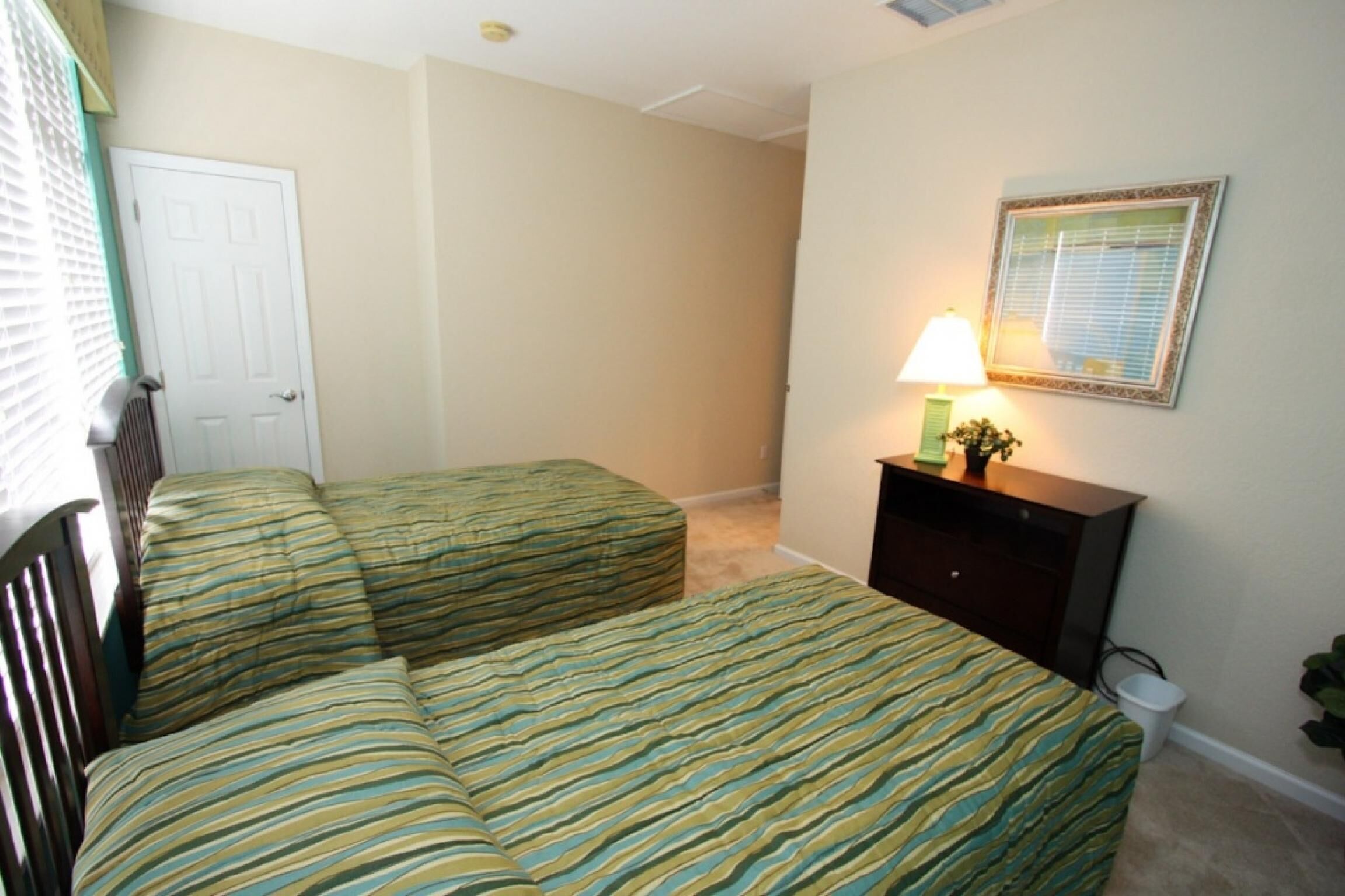 A bedroom with two beds, a dresser, a lamp, and a door.