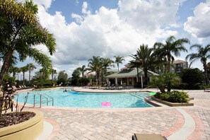 A swimming pool with lounge chairs and palm trees, surrounded by a paved area and a building in the background. - 5048 Vista Cay (Orlando)
