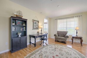 A living room with a bookshelf, a desk, two chairs, a patterned rug, and a large window with curtains. - 5048 Vista Cay (Orlando)