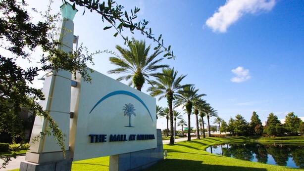 A sign for The Mall at Millenia with a palm tree logo, surrounded by well-maintained grass and palm trees. - 721 Terrace Ridge (Davenport)
