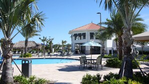 A pool area with lounge chairs, a dining table, and a building with a red roof. - 4888 Storey Lake (Kissimmee)