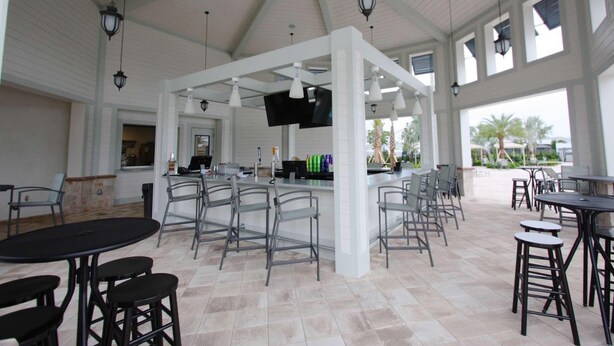 An indoor patio area with a bar, multiple tables and chairs, and a television screen. - 4888 Storey Lake (Kissimmee)