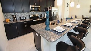 A modern kitchen with dark cabinets, granite countertops, and stainless steel appliances. There is a central island with bar stools and a decorative blue vase. - 4888 Storey Lake (Kissimmee)