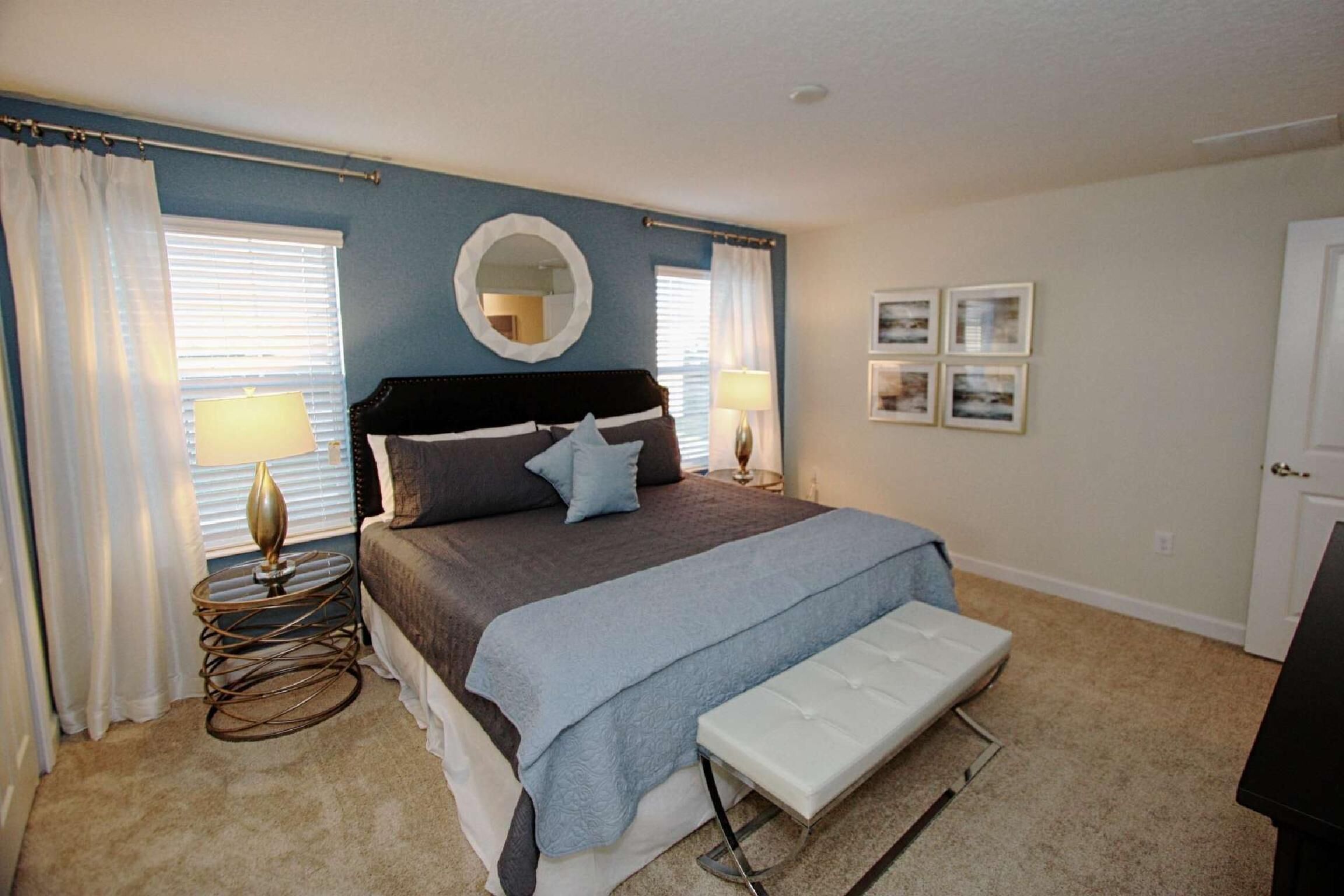 A bedroom with a bed, bedside lamps, a round mirror, and a bench.