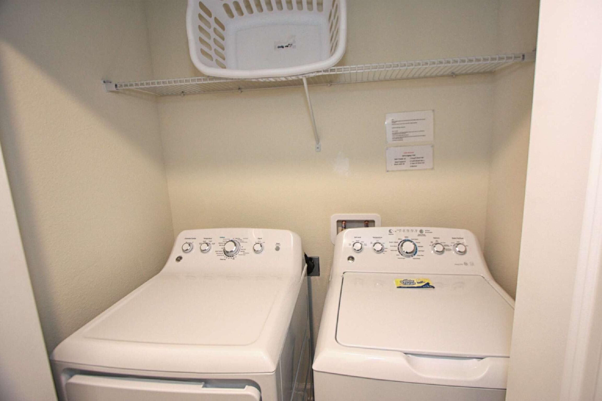 A laundry room with two front-loading washing machines and a white laundry basket on a shelf.