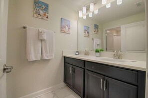 A bathroom with a double sink vanity, dark cabinets, a large mirror, and decorative wall art. - 1566 Champions Gate (Davenport)