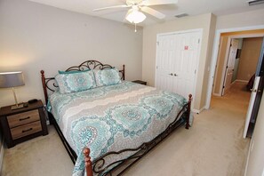 A bedroom with a bed, a nightstand, a lamp, a ceiling fan, and a door. - 3175 Encantada (Kissimmee)