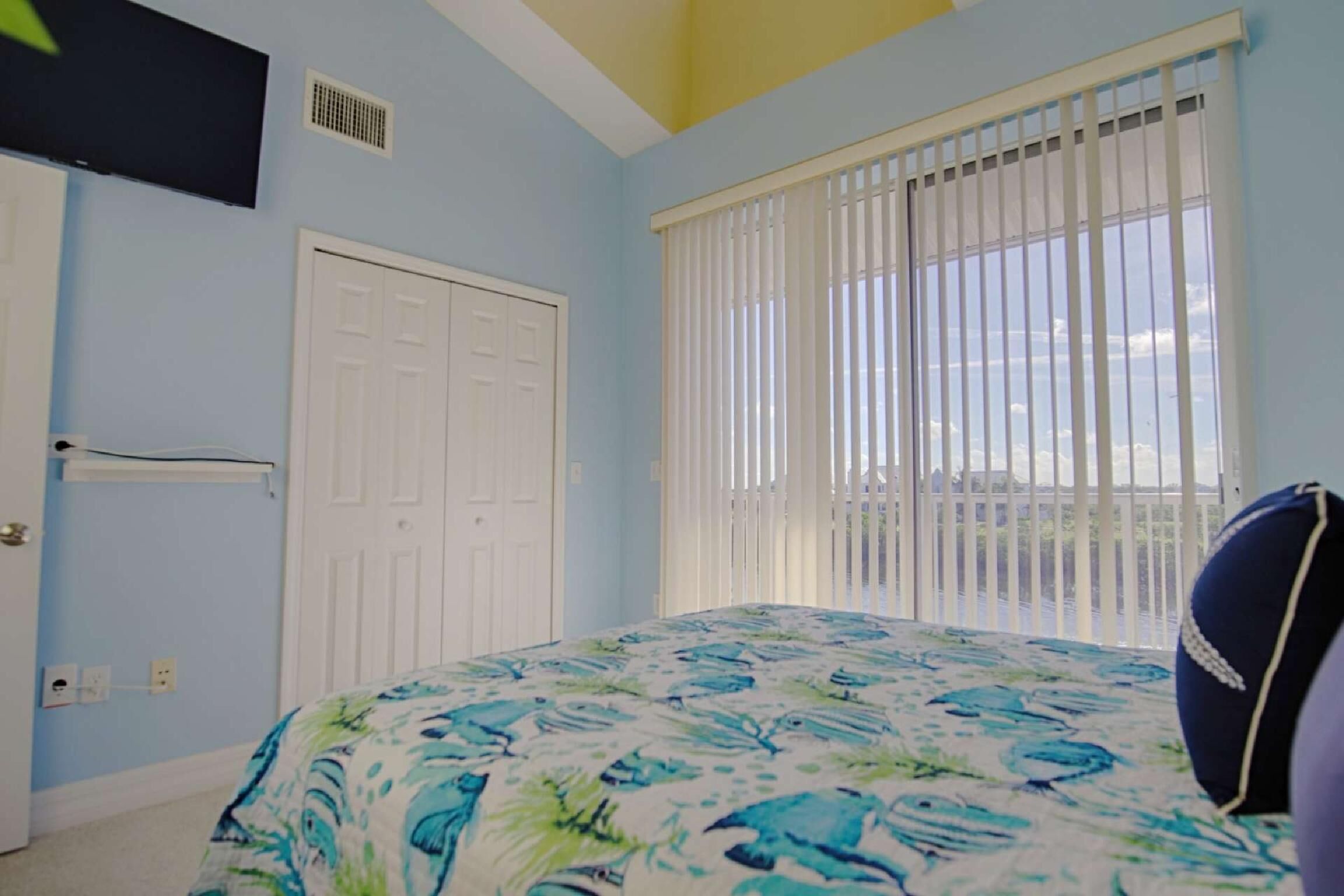 A bedroom with a bed, a window with blinds, a door, and a ceiling vent.