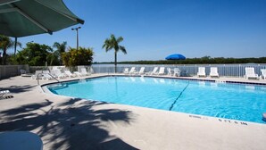Una piscina cristallina azzurra con lettini bianchi e un cartello che indica divieto di tuffi.