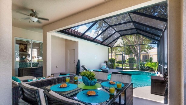 Um pátio externo com estrutura de vidro, móveis de vime, piscina e vista da região.