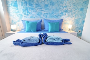 Een net opgemaakt bed met twee opgevouwen handdoeken, een wit hoofdeinde en twee bijpassende kussens.