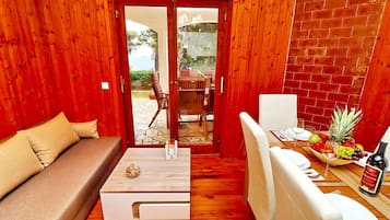 A cozy room with a wooden interior, a sofa, a dining table with a fruit basket, and a bottle of wine.