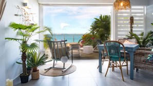 A modern living room with a view of the ocean, featuring a dining table, chairs, and potted plants. - Apartment on the beach (Grand-Case)