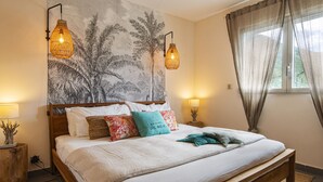 A bedroom with a large bed, two bedside lamps, a wall tapestry, and a window with curtains. - Apartment on the beach (Grand-Case)
