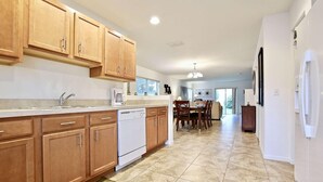 A spacious kitchen with wooden cabinets, a dishwasher, and a dining area with a table and chairs. - 5113 Compass Bay (Kissimmee)