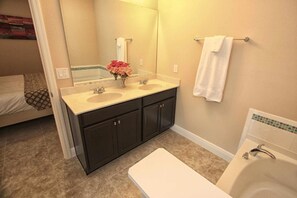 A bathroom with two sinks, a large mirror, a bathtub, and a toilet. - 5303 Solterra (Davenport)