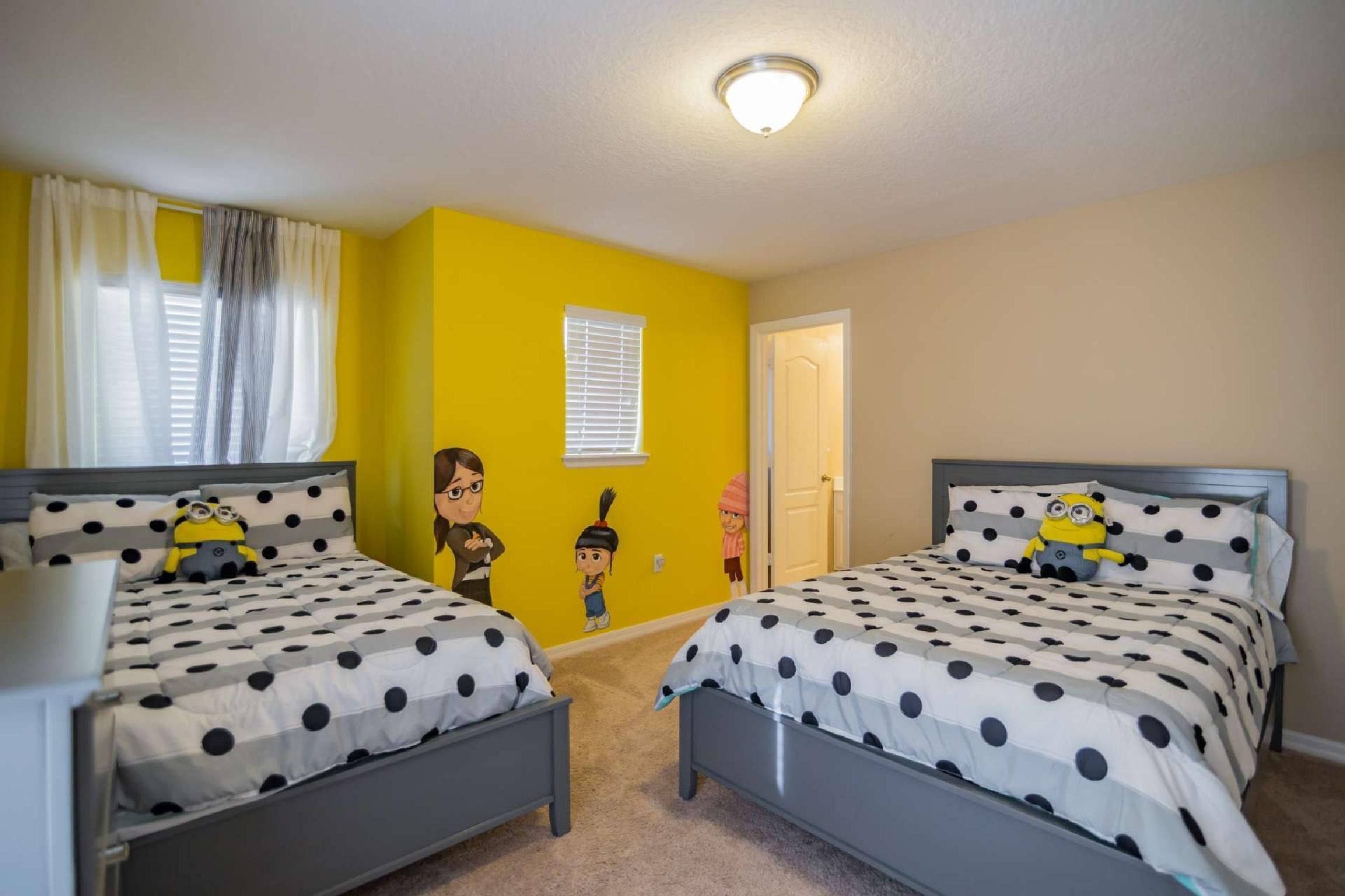 Un dormitorio con dos camas, cada una con una colcha de lunares y almohadas a juego. Las paredes son amarillas, el techo es blanco y hay una puerta que da a otra habitación.