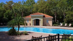 A building with a tiled roof, a pool, and a surrounding area with trees and lounge chairs. - 3207 Compass Bay (Kissimmee)
